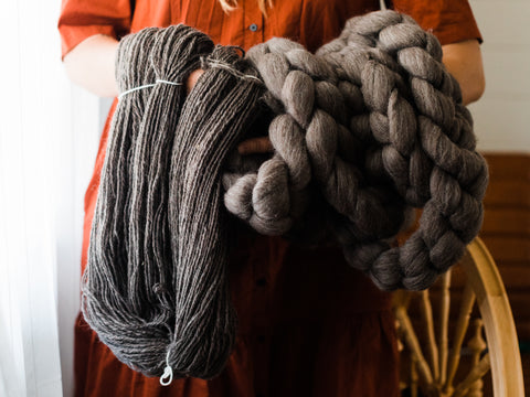 arms holding skeins of handspun yarn and unspun charcoal coloured combed top