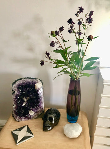 A large amethyst geode displayed on a shelf with a vase of flowers