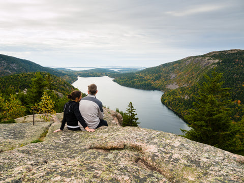 A couple sitting atop a mountain overlooking Jordan Pond Lake in Acadia National Park