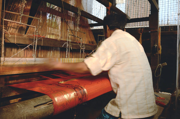Indian man weaving on handloom orange gold fabric
