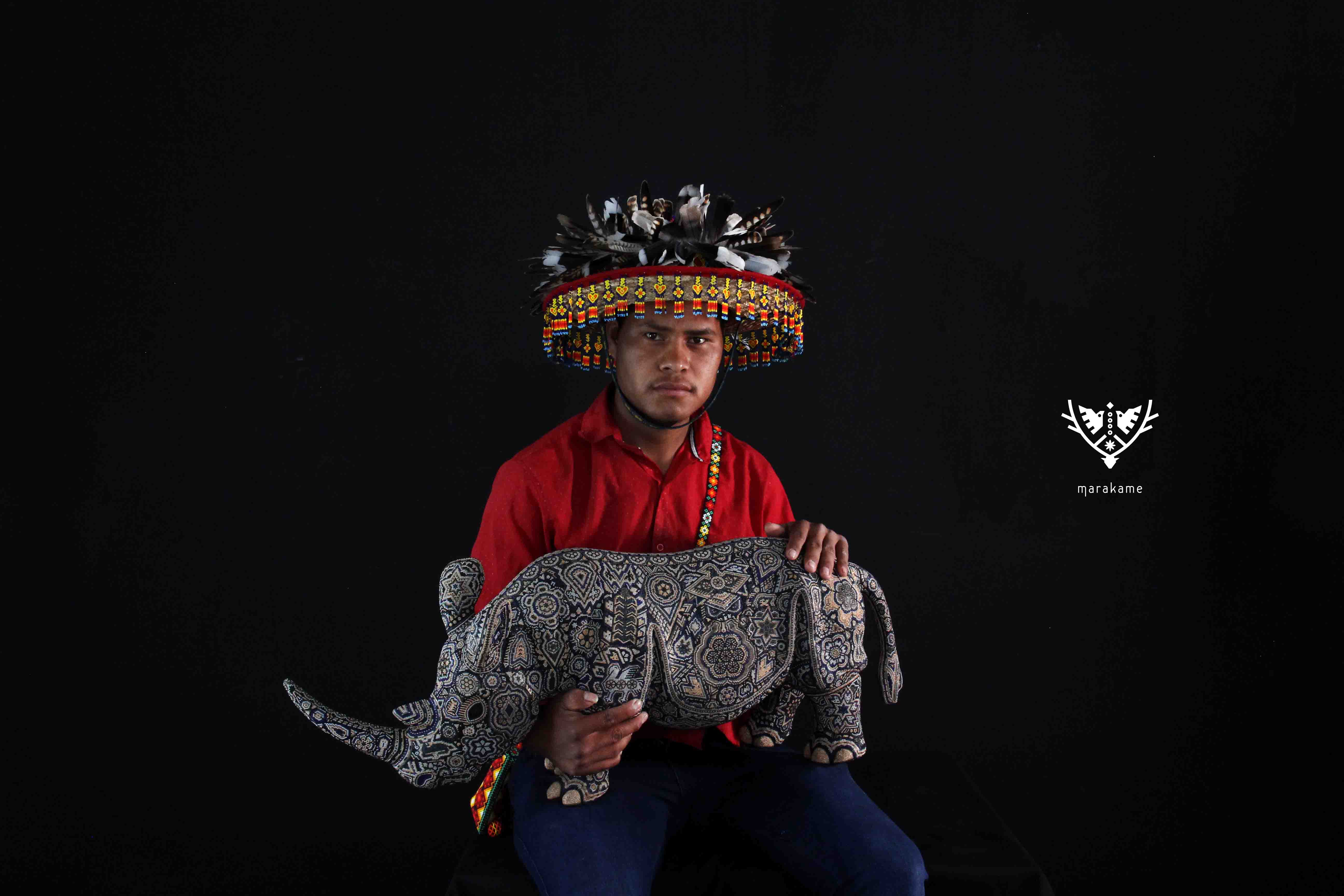 Artista wixarika cargando rinoceronte intervenido con chaquira de cristal y pegamento epóxico.