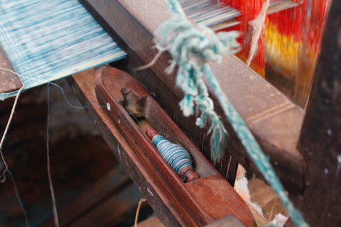 A close up of a loom with a shuttle and blue coloured yarn