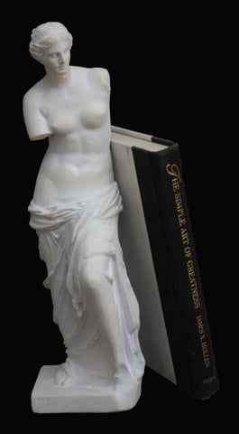 Photo with black background of plaster cast of partially nude female and a black and tan book leaning against it