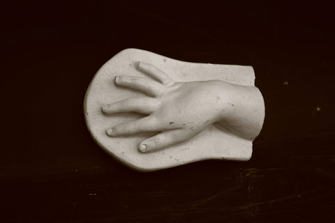 photo of plaster cast of baby hand on low panel with black background
