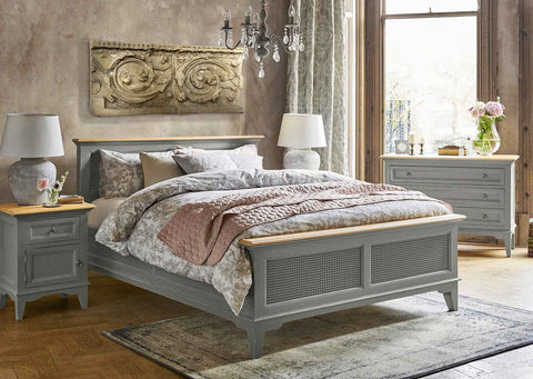 photo of bedroom with gray matching bed, side tables with lamps, and bureau, floral bedding and curtains, oriental rug on wood floor, chandelier, and plaster cast relief sculpture of architectural scrollwork above bed