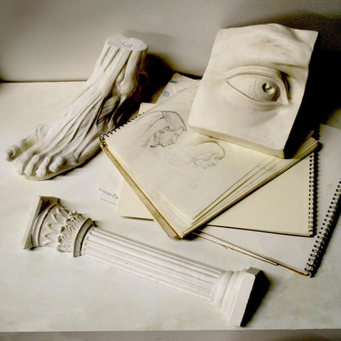 Photo of a plaster cast sculpture of David's eye, a foot, and a column on a stack of sketchbooks on a white table