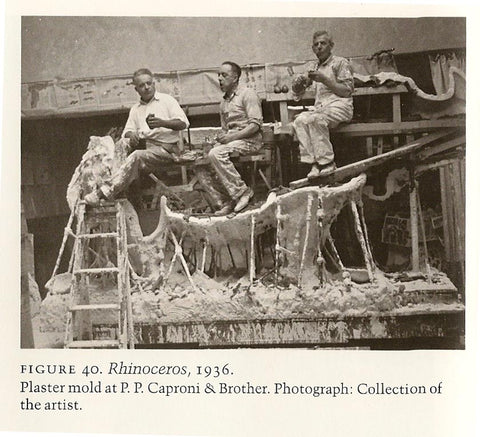 black and white photo of three men eating lunch inside frame of large plaster mold of a rhino