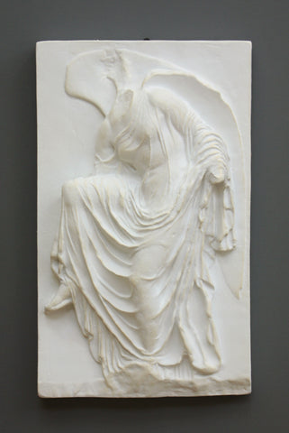 photo of cast of sculpture relief of robed figure, head now missing, reaching for her sandal in White Patina on a dark gray background