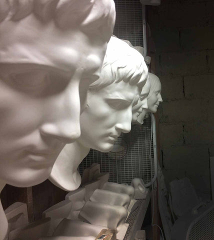 photo of several plaster cast masks hanging in a row with more plaster casts on a shelf and box fans