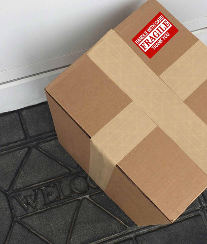 photo of brown package with red fragile sticker on a doorstep with a black welcome mat