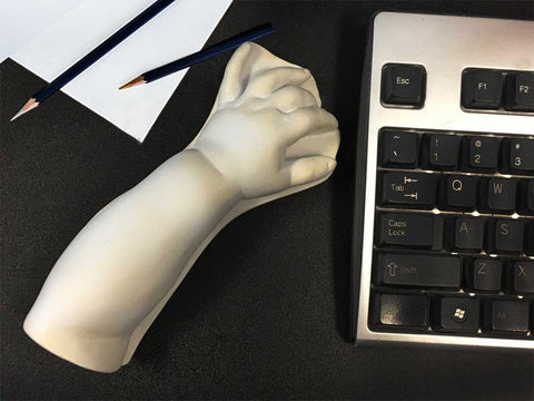 photo of plaster cast of baby arm past the elbow sitting on a desk between a keyboard on the right and a sheet of paper and two drawing pencils on the left