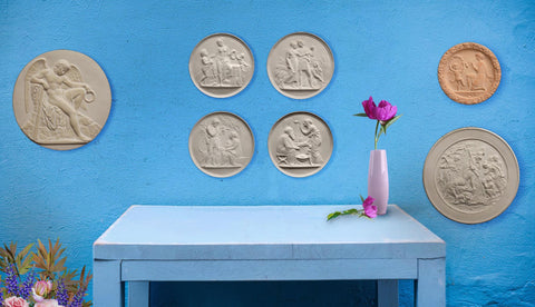 Photo of 7 Round Plaster Cast Relief Sculptures on a blue wall above a desk with a vase and pink flower