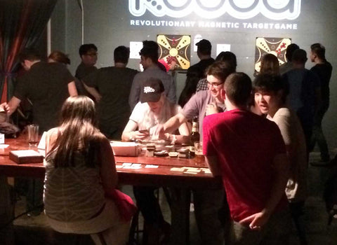 People sat playing table top games with others playing KOOBA against a wall in the background