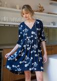 [Color: Navy/Ivory] A model wearing a flowy navy blue bohemian mini dress with floral embroidery.