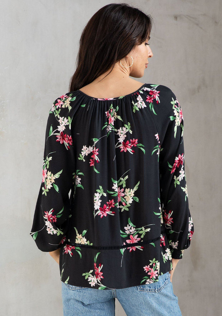 [Color: Black/Red] A model wearing a gorgeous black bohemian blouse in a pink floral print. With long sleeves and a split v neckline with tassel ties. 