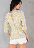 [Color: Blue/Lemon] A model wearing a blue and yellow retro floral print peplum top with a tie front detail. 