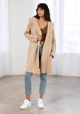 [Color: Taupe/Cream] A model wearing a cozy taupe oversize mid length cardigan. With side pockets, an open front, a shawl collar, and a hoodie. 