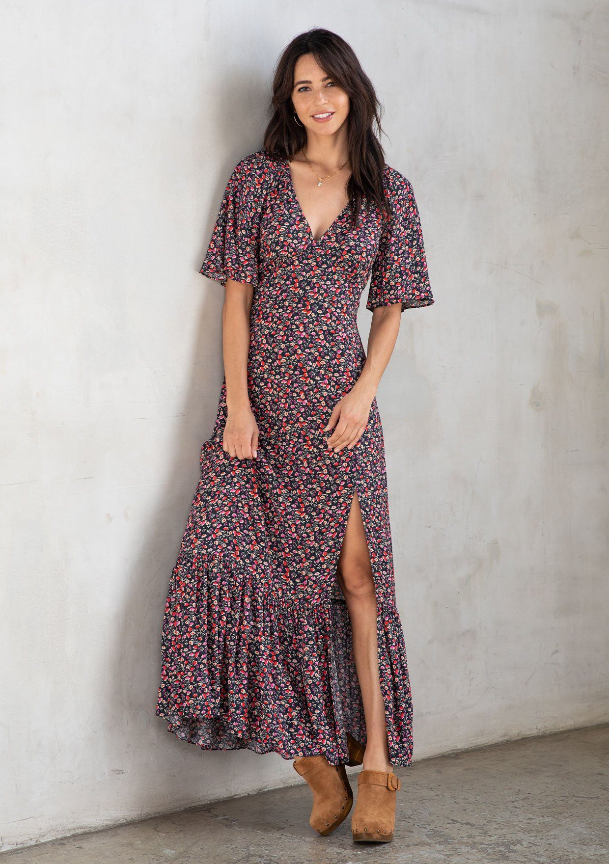 [Color: Black/Fuchsia] A model wearing a timeless flowy bohemian maxi dress in a black and fuchsia ditsy floral print. With short flutter sleeves, a deep v neckline, and a leg baring side slit.