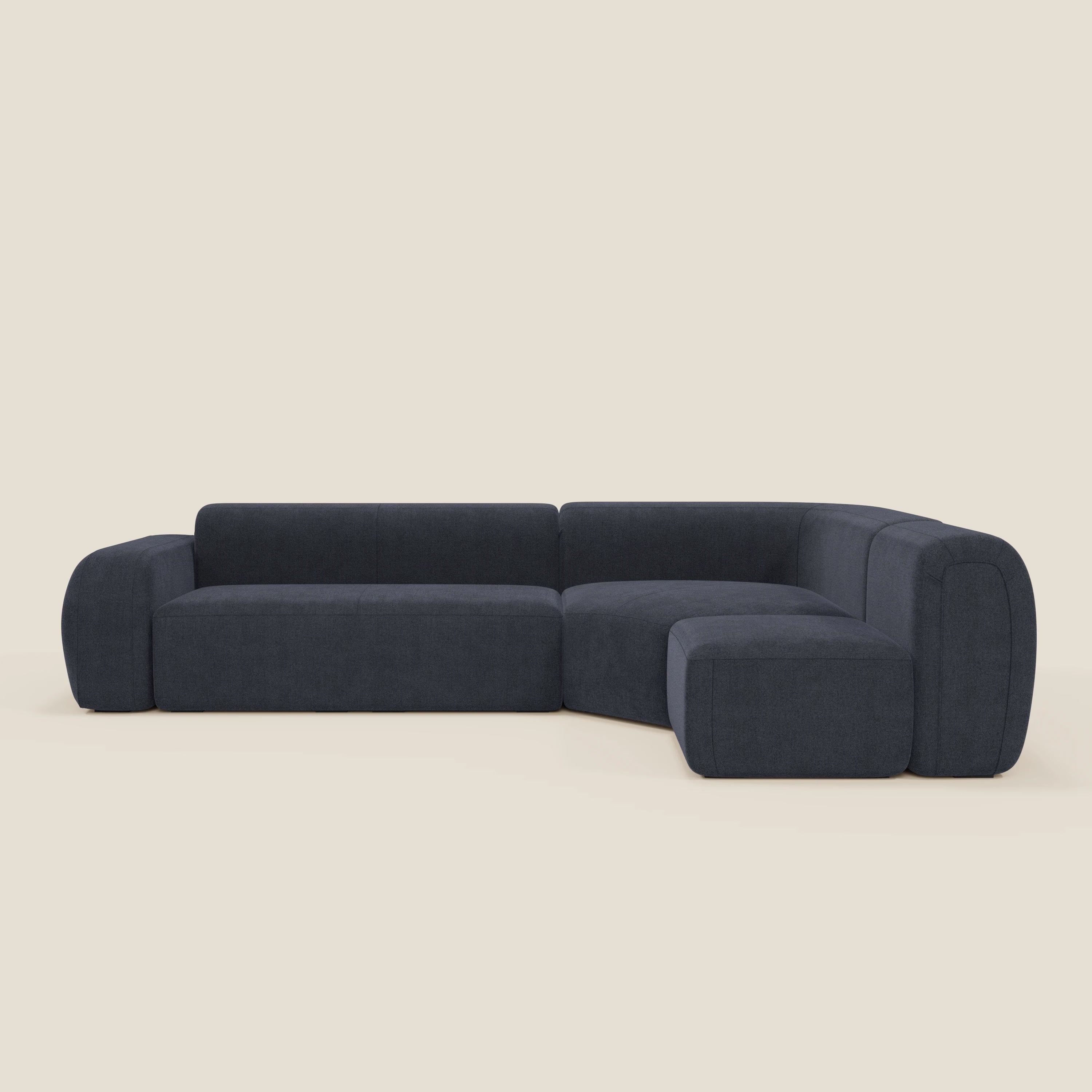 Il divano angolare componibile e modulare BonBon di Divani.Store, in tessuto antimacchia T23 ardesia blu, è caratterizzato da una moderna forma a L con bordi arrotondati, sedute basse e larghe, cuscini morbidi e design minimalista su sfondo beige chiaro.