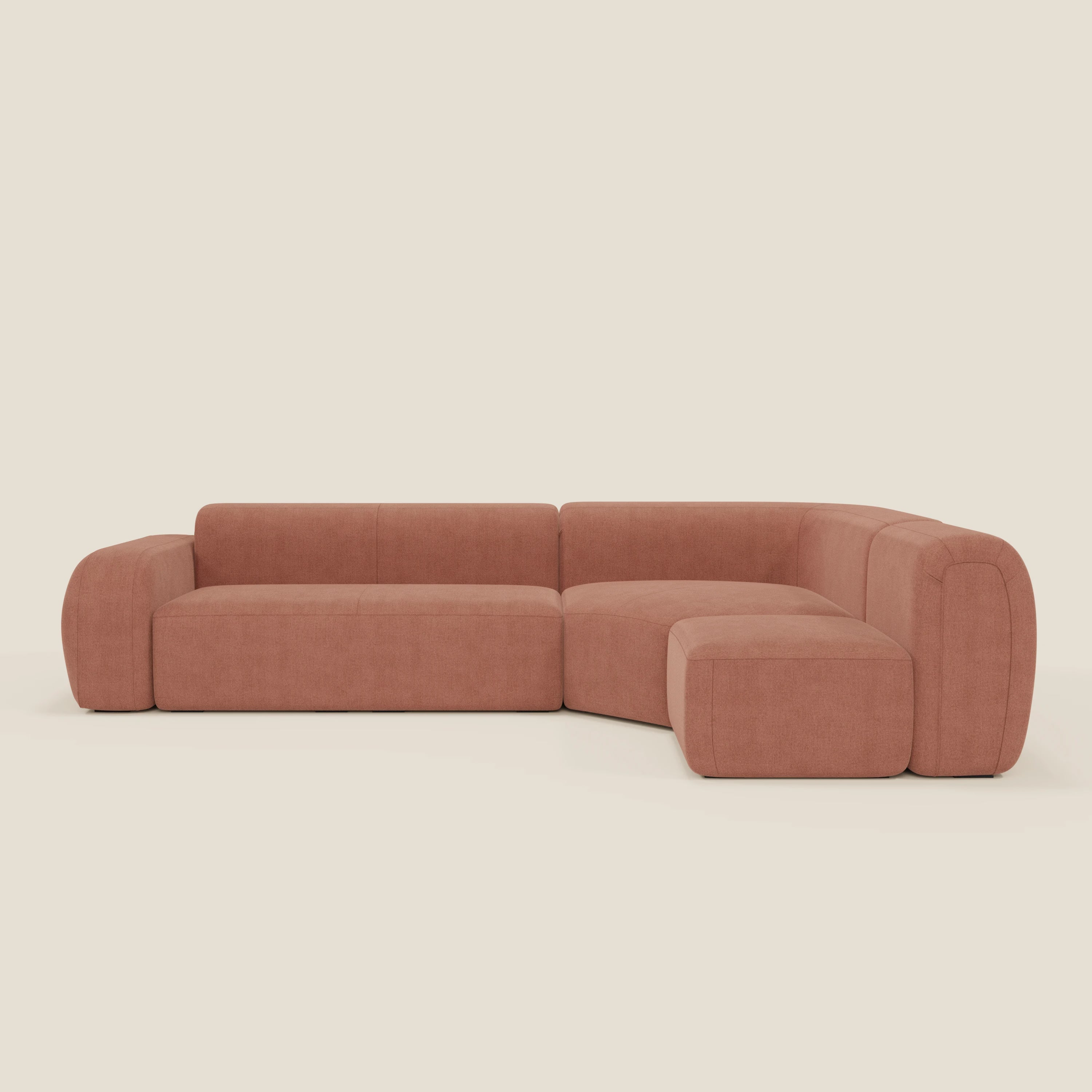 Il divano BonBon angolare componibile e modulare di Divani.Store è caratterizzato da braccioli e schienali ampi e arrotondati in tessuto smacchiabile T23 pesca, con sedute profonde e cuscini morbidi, su uno sfondo in tinta unita color crema chiaro.