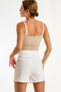 Falda short de corte en a, cintura alta con pretina, sobrefalda frontal con abertura y cierre con cremallera visible posterior.