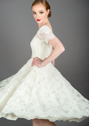 Nina is a tea length vintage inspired lace dress with oﬀ the shoulder neckline and trimmed with a satin bow belt