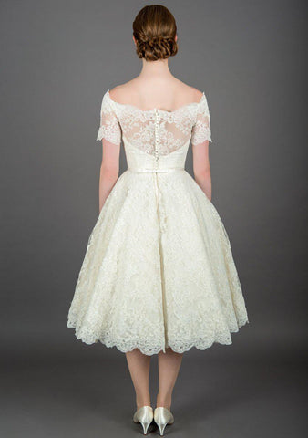 Rear view of Nina tea length vintage inspired lace dress with oﬀ the shoulder neckline and trimmed with a satin bow belt