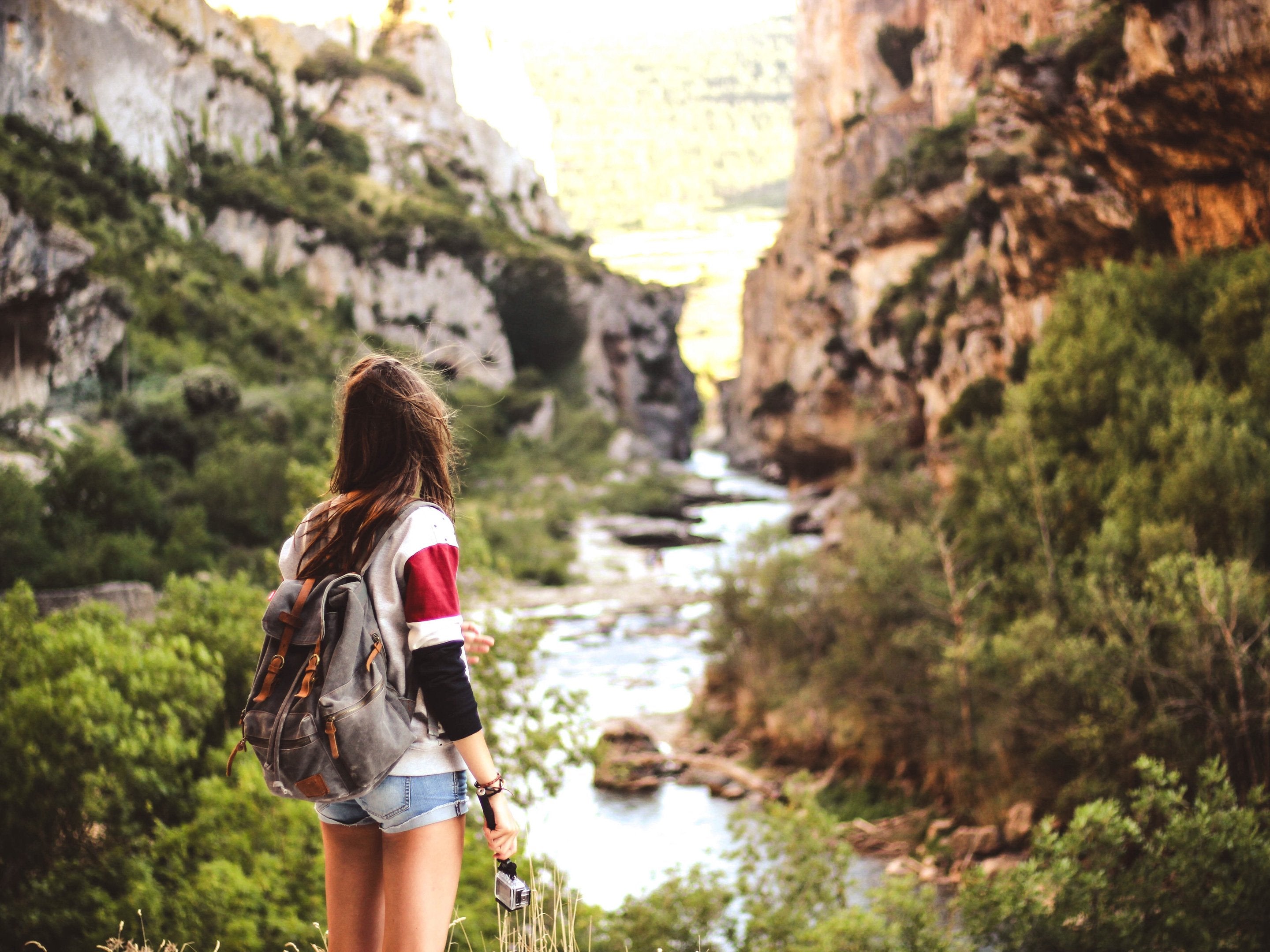 Brewed to save the planet - Woman with backpack hiking by a stream among mountains