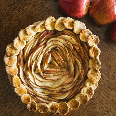 baked apple pie with spiral pattern made from apples, fresh whole apples on the side