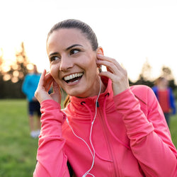 Think Clearer – Young woman outdoors with earbuds in ears and smiling