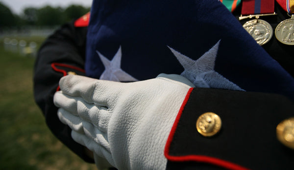 Close-up of military member’s hands in Dress Blues holding a folded American flag.