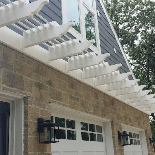 Picture of an eyebrow pergola with 5 purlins a few feet above 2 single garage doors
