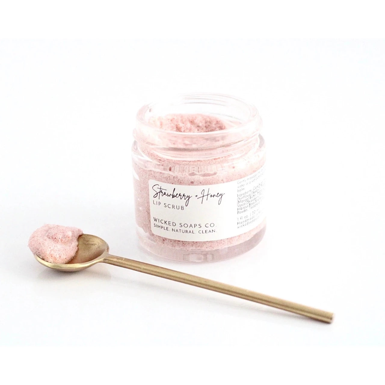 A small glass jar holds light pink strawberry and honey lip scrub. By Wicked Soaps Co.