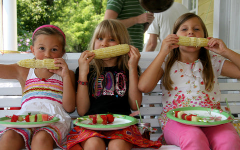 three girls eating corn on a porch swing at a summer party
