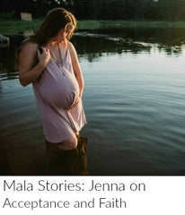 A pregnant woman with long auburn hair stands in a river with a wet pink sundress. She is wearing a sandalwood mala bead necklace from Mama Malas