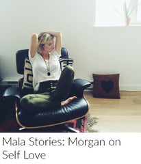 A blonde woman in a white tshirt and jeans relaxes with her arms above her head in a black lounge chair. She is wearing a sandalwood, black onyx and amazonite mala bead necklace from Mama Malas.