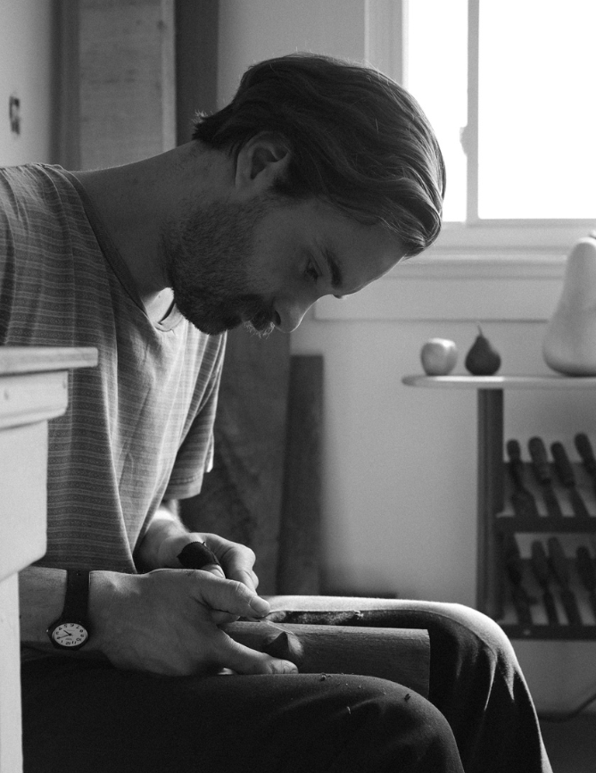 Black and white photograph of artist Ashley Jospeh Martin carving a wooden sculpture