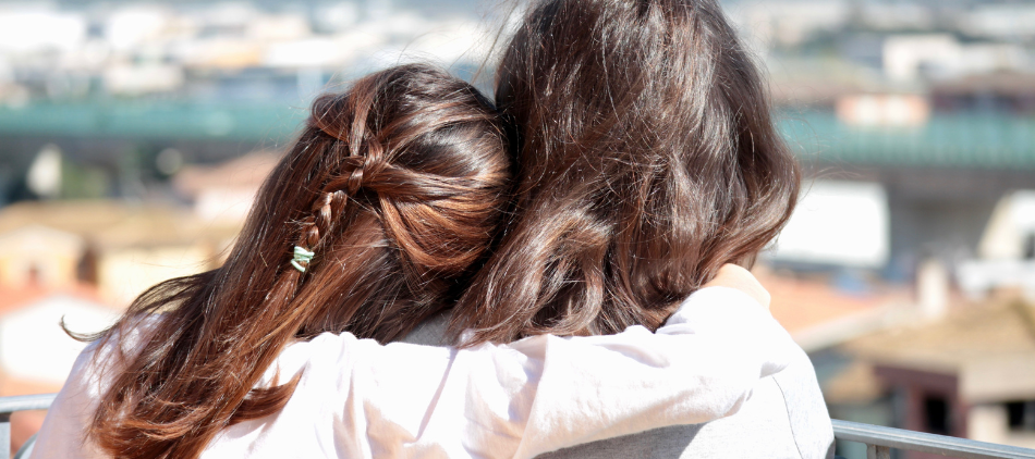 Two people with arms around each other, viewed from behind