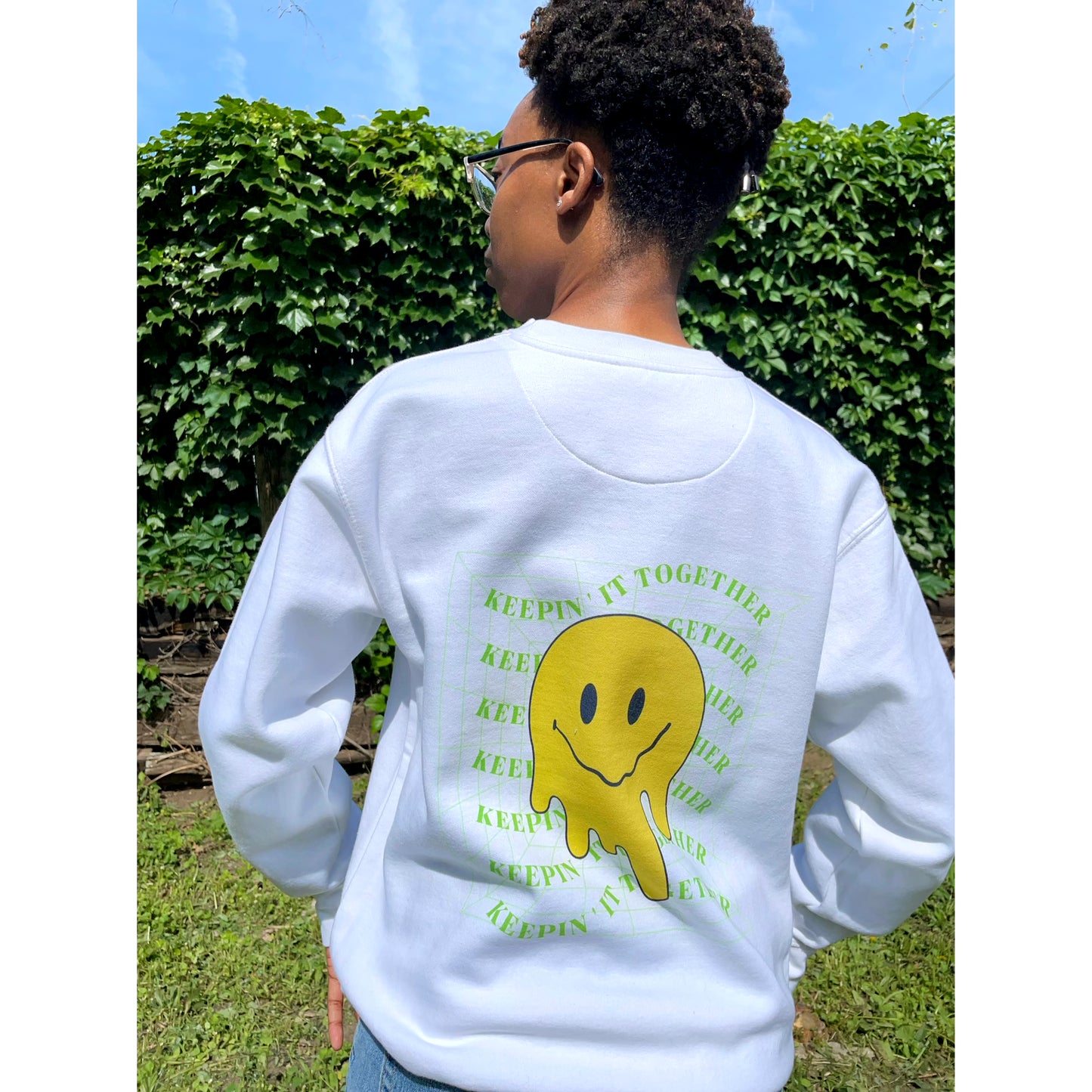 back view of white pullover sweatshirt with green "keepin it together" text on front and back with melting smiley face