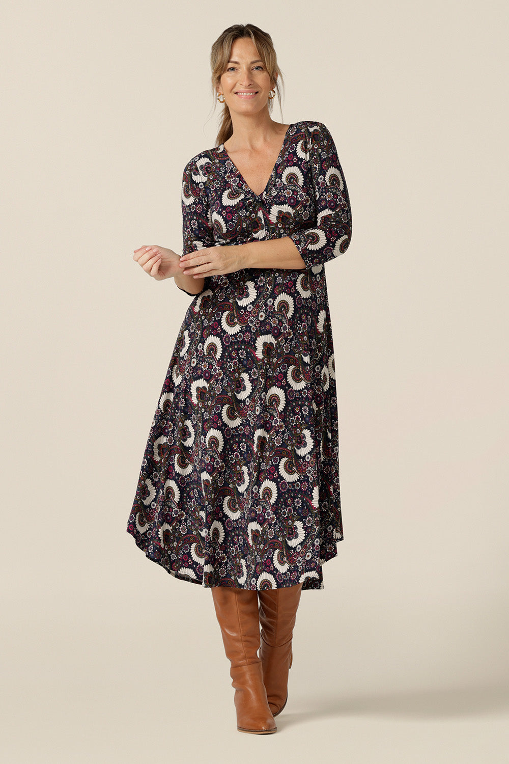 A size 10, 40 plus woman wears a 3/4 sleeve empire line dress with twist front bodice ad dipped, calf length hem. Made in Australia by Australian and New Zealand women's clothing brand, L&F this paisley print jersey dress is available to shop in sizes 8 to 24.  