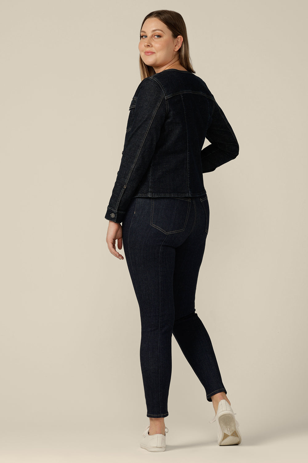 Back view of a collarless denim jacket in size 12 is worn with white bamboo jersey T-shirt and super-stretch skinny jeans. Consciously made in partnership with Outland Denim, this denim jacket is tailored to fit women in sizes 8 to 24 by Australian and New Zealand women's clothing experts, L&F.