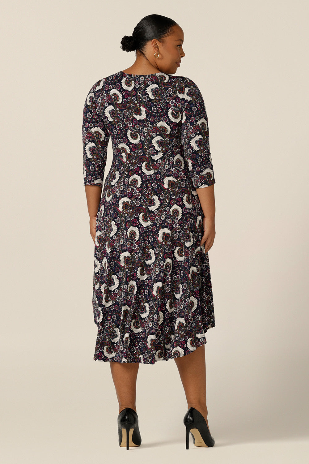 Back view of a size 18, plus size woman wearing a 3/4 sleeve empire line dress with twist front bodice ad dipped, calf length hem. Made in Australia by Australian and New Zealand women's fashion label, L&F this paisley print jersey dress is available to shop in petite to plus sizes.