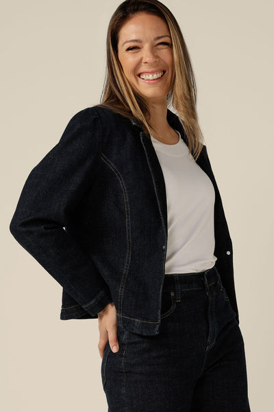 A size 8 woman wears a blazer-style jacket in midnight denim by Australian and New Zealand women's clothing label, L&F. Worn with high-waisted, flared cut jeans in comfort stretch, sustainable denim, this denim jacket is tailored to fit sizes 8 to 24.