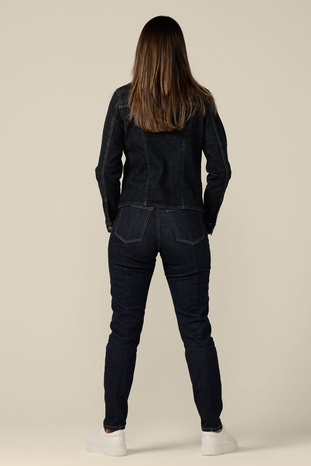 Back view of a collarless denim jacket in size 8 is worn with white bamboo jersey T-shirt and super-stretch skinny jeans. Ethically and sustainably made in partnership with Outland Denim, this denim jacket is tailored to fit women in sizes 8 to 24 by Australian and New Zealand women's clothing label, L&F.