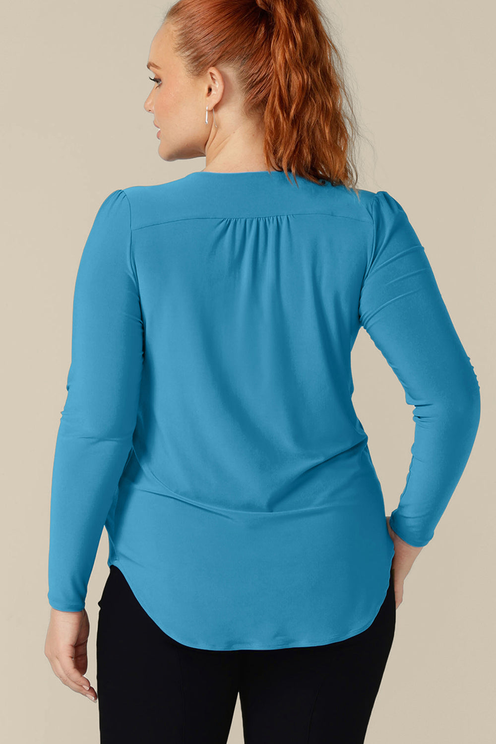 Back view of a size 12, curvy woman wearing a long sleeve, V-neck top in Opal blue jersey. Made in Australia by Australian and New Zealand women's clothing company, L&F, shop tops in inclusive sizes, 8 to 24 with free shipping to New Zealand. 