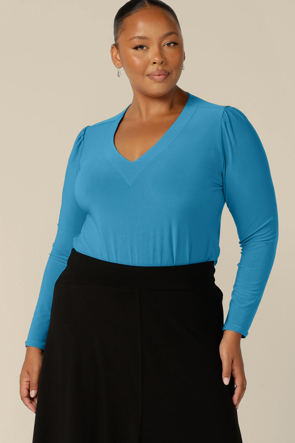 A plus size, size 18 woman wears a long sleeve, V-neck top in Opal blue jersey. Made in Australia by Australian and New Zealand women's clothing company, L&F, this top is available for shipping in sizes 8 to 24.