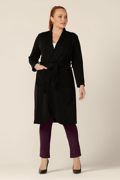 Great for chic city style, this black coat layers well for commuter workwear and travel. A curvy size 12 woman wears this softly tailored black trenchcoat in modal fabric with mulberry slim leg pants and a white bamboo jersey top.