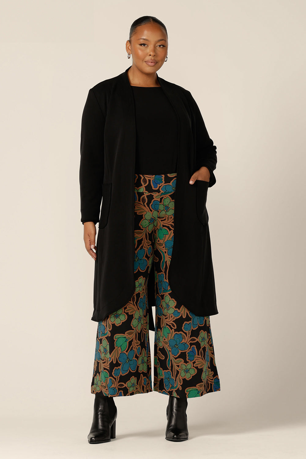 Great for chic city style, this black coat layers well as a commuter work wear and coat for travel. Worn by a fuller figure, size 18 woman, this softly tailored black trenchcoat in modal fabric is worn with printed jersey, wide leg pants and a black boat neck top.