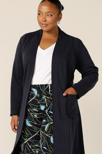 A size 18 woman wears the Marant Trenchcoat in Bluestone by Australian and New Zealand size inclusive clothing brand, L&F. A collarless, open fronted coat with tie belt and patch pockets, this classic navy coat is made in Australia. 