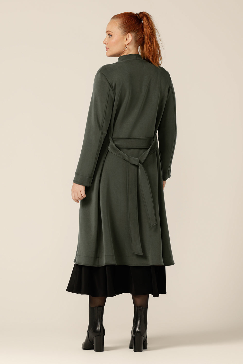 Back view of a size 12 woman wearing the Marant Trenchcoat in Sage green by Australian and New Zealand women's clothing label, L&F. A collarless, open fronted coat with tie belt and patch pockets, this warm coat in stretchy modal fabric is worn with a 3/4 sleeve, reversible black dress.